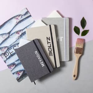 A collection of notepads in grey and beige with a paintbrush and leaves on a light background.