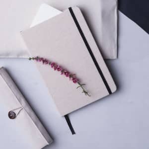 A light beige notepad with a black elastic band, featuring a floral design on the cover. It includes a white insert.