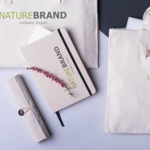 A beige notepad with a floral design lies on a grey surface, accompanied by a pencil case and tote bag.