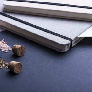 A set of Telmak notepads in black and white, featuring elastic bands, with some spices and cork stoppers nearby.