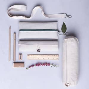 A beige pencil case with a green zipper, surrounded by pencils, a ruler, a sharpener, a flower, and a strap.
