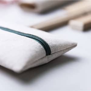 A beige pencil case with a green zipper, accompanied by wooden items in a blurred background.