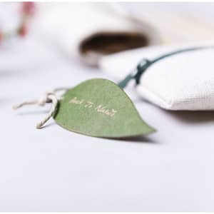 A white pencil case with a green tag attached, featuring a branding logo. Decorated with a natural aesthetic.