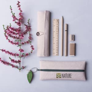 A cream pencil case with a green zipper, containing a pencil, ruler, pen, sharpener, and eraser, alongside a flower.