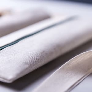 A pencil case in a natural, off-white fabric with a green zipper and a strap. The case has a simple, minimalist design.