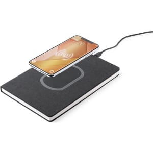 A black notepad with a wireless charging area, featuring a smartphone placed on top and a charging cable connected.