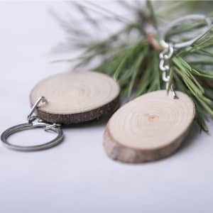 Two wooden keyrings with a natural finish, attached to metal chains, resting among green pine branches.