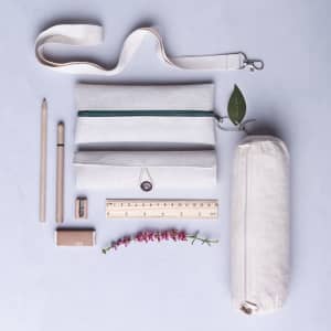 A collection of beige canvas pouches, a ruler, pencils, a pen, a sharpener, and a flower, featuring a strap.