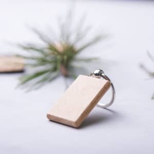 A wooden keyring with a metallic attachment, placed on a light background with greenery nearby.