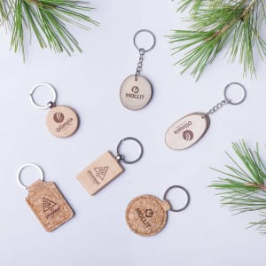 A collection of wooden and cork keyrings featuring various shapes and a metal keyring attachment, surrounded by foliage.