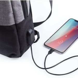 A grey and black shoulder bag with a USB charging port, connected to a smartphone.