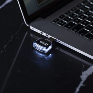 A black and silver Novuk 16Gb USB memory stick plugged into a laptop, with a glowing light.