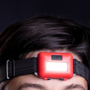 A red headlamp mounted on a black adjustable strap, positioned on a person's forehead.