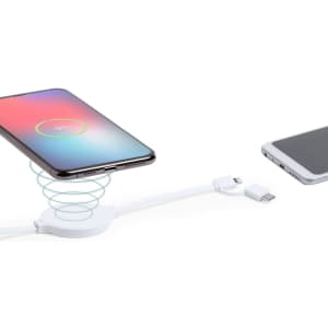 A white wireless charger with a smartphone placed on it and a charging cable beside it.