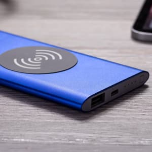 A blue power bank with a wireless charging surface and multiple ports, placed on a wooden surface.