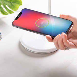 A white multifunction lamp with a wireless charging base, featuring a smartphone displaying a charging indicator.