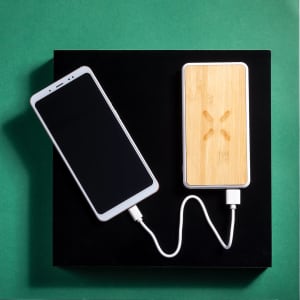 A power bank with a bamboo finish connected to a smartphone via a white charging cable, set against a green background.