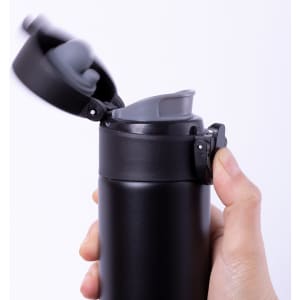 A drink bottle with a sleek black exterior and a grey lid, featuring an opening mechanism, held in a hand.