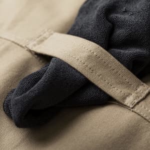 A close-up of a tan apron featuring a black fabric loop secured with a tan strap. Includes a logo detail.