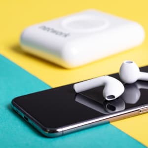 A white power bank rests on a smartphone, with matching white earphones placed nearby on a vibrant yellow and teal background.