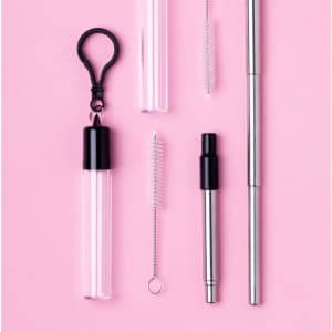 A collection of silver and clear drinking straws, a cleaning brush, and a case with a clip, set against a pink background.