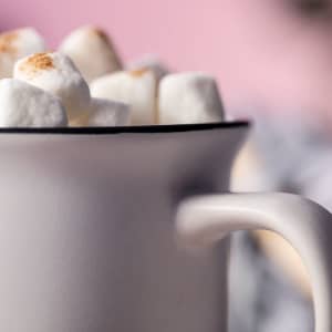 A white coffee mug with a black rim filled with fluffy marshmallows.