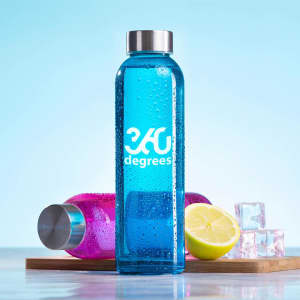 A drink bottle in bright blue, featuring a logo, beside a pink bottle, lime, and ice on a wooden surface.
