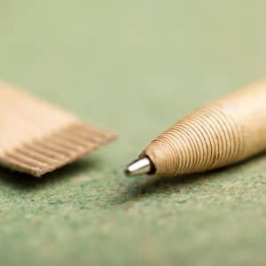 A gold-coloured pen with a metallic tip, alongside its cap, displayed on a textured green surface.