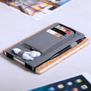 A grey charger organizer with space for cards, a pen, and earbuds, placed on a cork notebook.