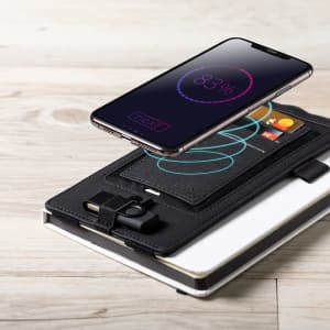A wireless charger in black with a phone and card slots, featuring a logo and a sleek design on a wooden surface.