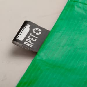 A green reusable grocery bag with a label featuring a logo and recycling symbol.