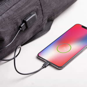 A grey backpack featuring a USB charging port, connected to a smartphone displaying a charging icon.