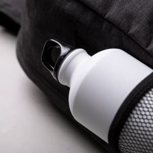 A white drink bottle is attached to a black backpack, featuring a mesh pocket for secure storage.