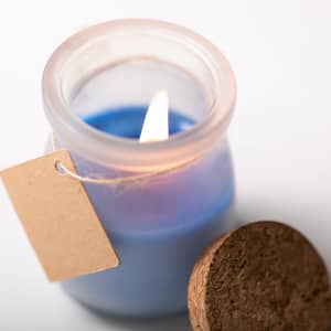 A blue aromatic candle in a clear glass jar with a cork lid and a tag attached.