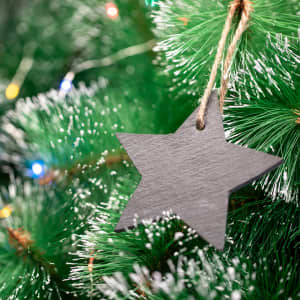 A black star-shaped decoration hanging from a green Christmas tree branch with twinkling lights.