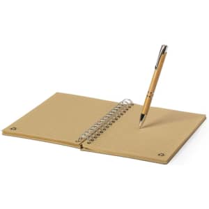 A tan spiral-bound notebook with lined pages and a silver pen resting on it. The notebook has a simple design with rounded corners.