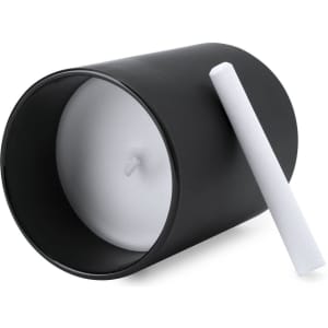 A black aromatic candle with a white wax interior and a wick, placed on its side with a white crayon beside it.