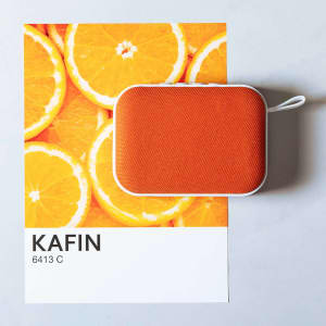 An orange Kafin Speaker on a white background featuring vibrant orange slices. The speaker has a compact design and a logo.