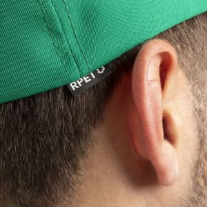 A green cap with a branding tag is seen close to the side of a person's head.