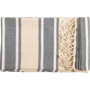 A folded towel pareo with a grey and cream striped design, featuring tassel detailing on one edge.