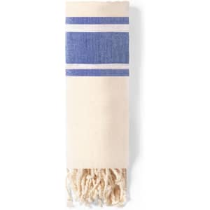 A towel pareo in cream with blue stripes and tassels at the end, featuring a logo.