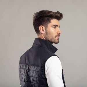 A man in a black puffer vest with a high collar, facing sideways against a neutral background.