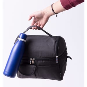 A black bag is held in one hand with a blue drink bottle attached to it. The bag features a front pocket and a handle.