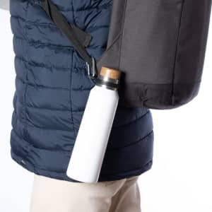 A white drink bottle is attached to a black bag via a strap, resting against a navy puffer jacket.