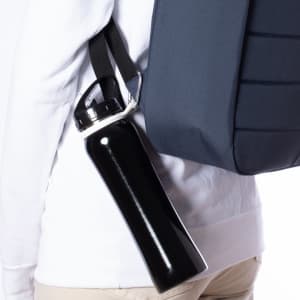 A black drink bottle with a silver cap held by a strap, attached to a navy backpack.