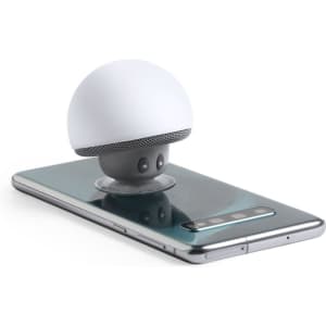 A compact white speaker with a rounded top sitting on a smartphone, featuring a grey base and visible branding.