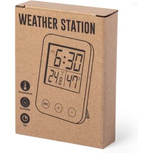 A weather station in a cardboard box featuring a digital display for time, temperature, and humidity. The box has a logo.