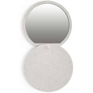 A round pocket mirror in a light grey colour with a speckled texture, featuring a reflective surface when opened.