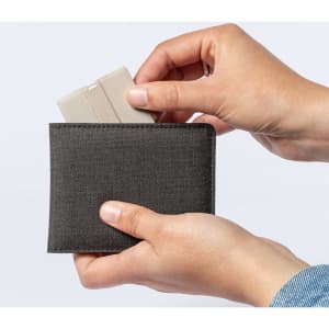 A grey wallet is held in hands, with a card being inserted into it. The wallet has a sleek, minimalist design.