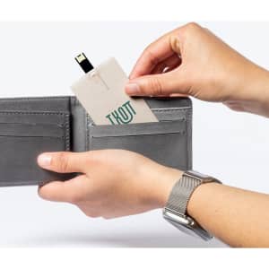 A grey USB flash drive is being inserted into a wallet, with a hand holding it and another hand supporting the wallet.